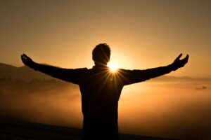 Person with their arms outstretched toward the setting sun