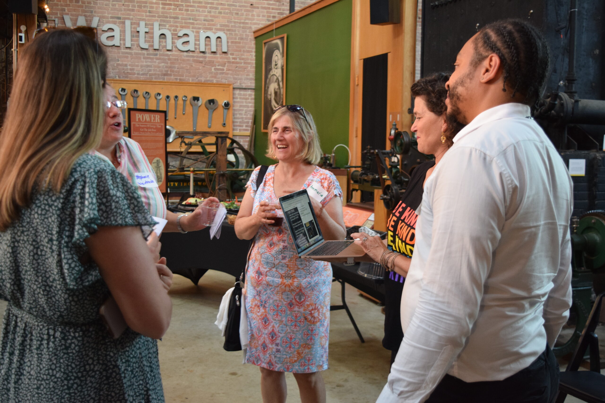 A group of five educators are standing in a group. One is smiling and conversing while the others listen